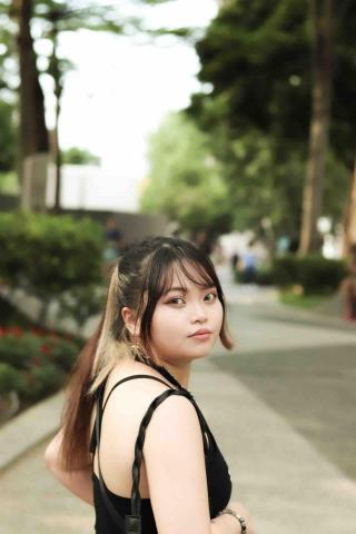 這張照片是一個年輕女子在戶外，她穿著黑色背心，留著棕色頭髮，看起來很自信。
